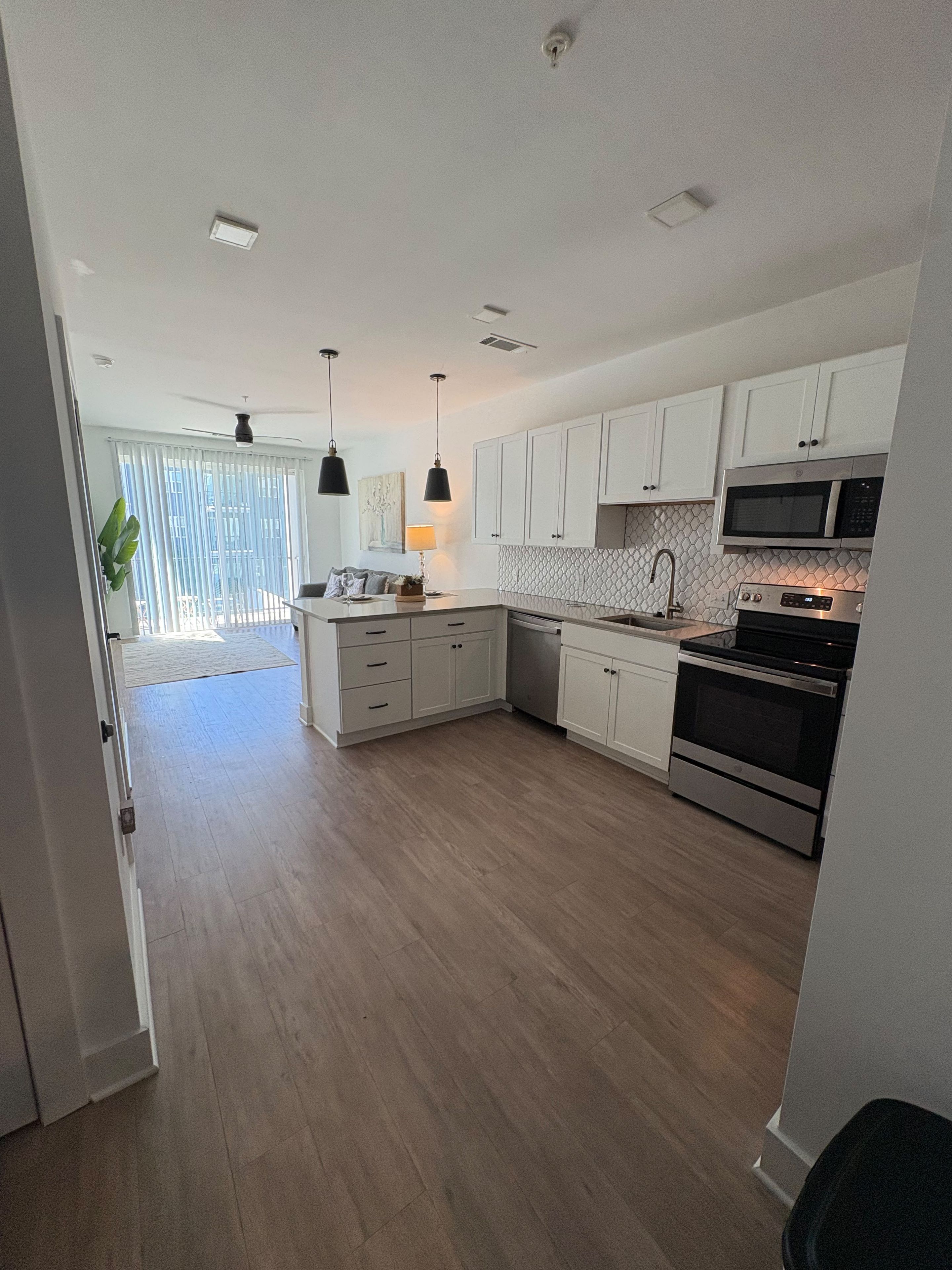 A modern kitchen with white cabinets, a microwave, an oven, and pendant lighting.