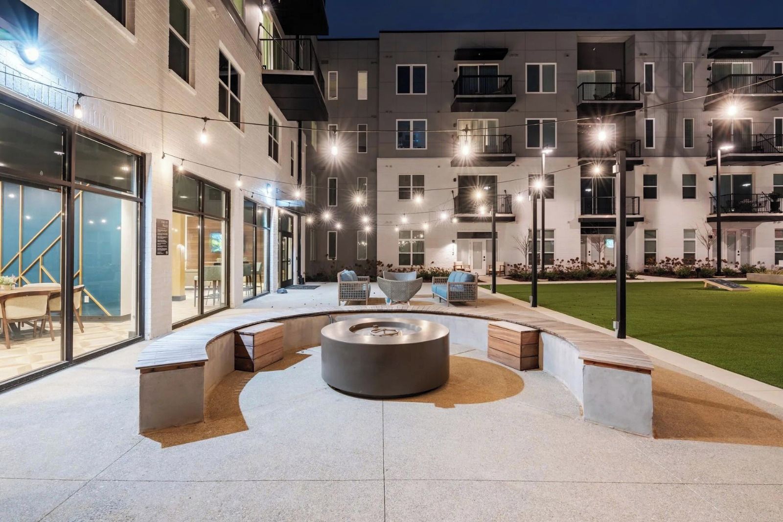 An outdoor patio area with a circular seating arrangement and a fire pit, surrounded by a building with multiple balconies and windows.