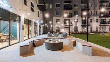 An outdoor patio area with a circular seating arrangement and a fire pit, surrounded by a building with multiple balconies and windows.