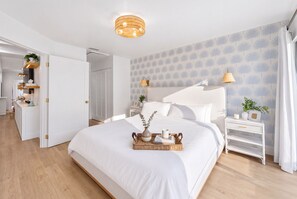 A modern bedroom with a large bed, a bedside table with a lamp, and a wall with a leaf pattern. - Marea - Key Largo Near Bay, Outdoor Lounge, Pool - Tennis Access (Key Largo)
