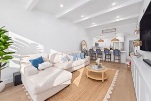A modern living room with a sofa, coffee table, and a dining area with chairs and a kitchen in the background. - Marea - Key Largo Near Bay, Outdoor Lounge, Pool - Tennis Access (Key Largo)