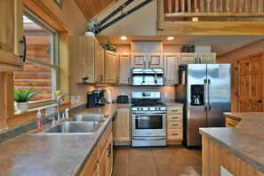 A modern kitchen with wooden cabinets, stainless steel appliances, and a large window. - Musky Haven-Your Northwoods Gathering Spot (Hayward)