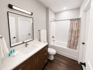 Ein modernes Badezimmer mit Waschbecken, Spiegel und Toilette, einem Holzkosmetikschrank und einer Dusche mit Duschvorhang.
