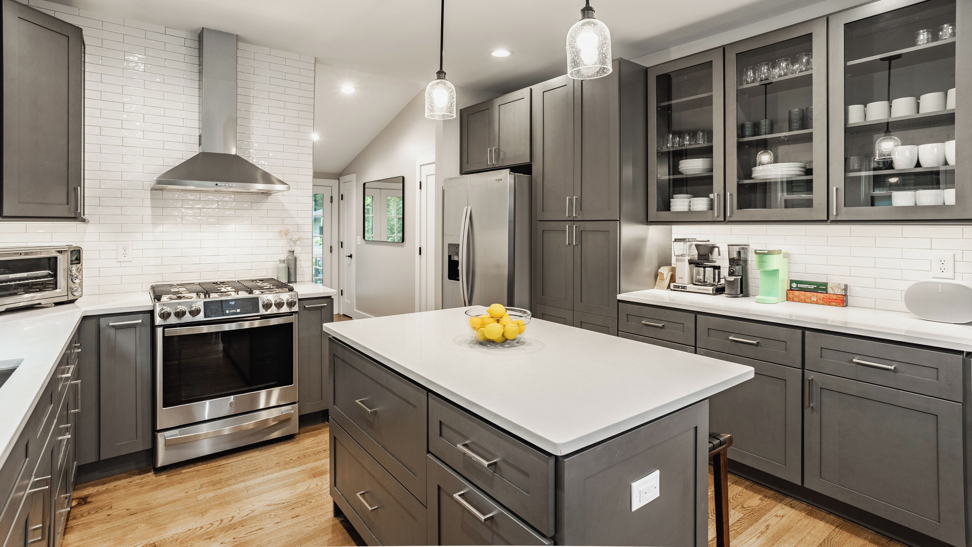 A modern kitchen with stainless steel appliances, grey cabinetry, and a central island with a bowl of lemons.