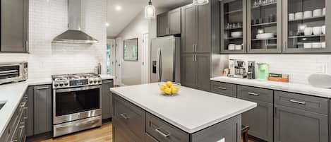 A modern kitchen with stainless steel appliances, grey cabinetry, and a central island with a bowl of lemons.