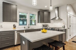 A modern kitchen with a central island, stainless steel appliances, and a window overlooking greenery. - This NEW "Old" House• Broad Ripple Home Steps From Dining, Nightlife & The Monon (Indianapolis)
