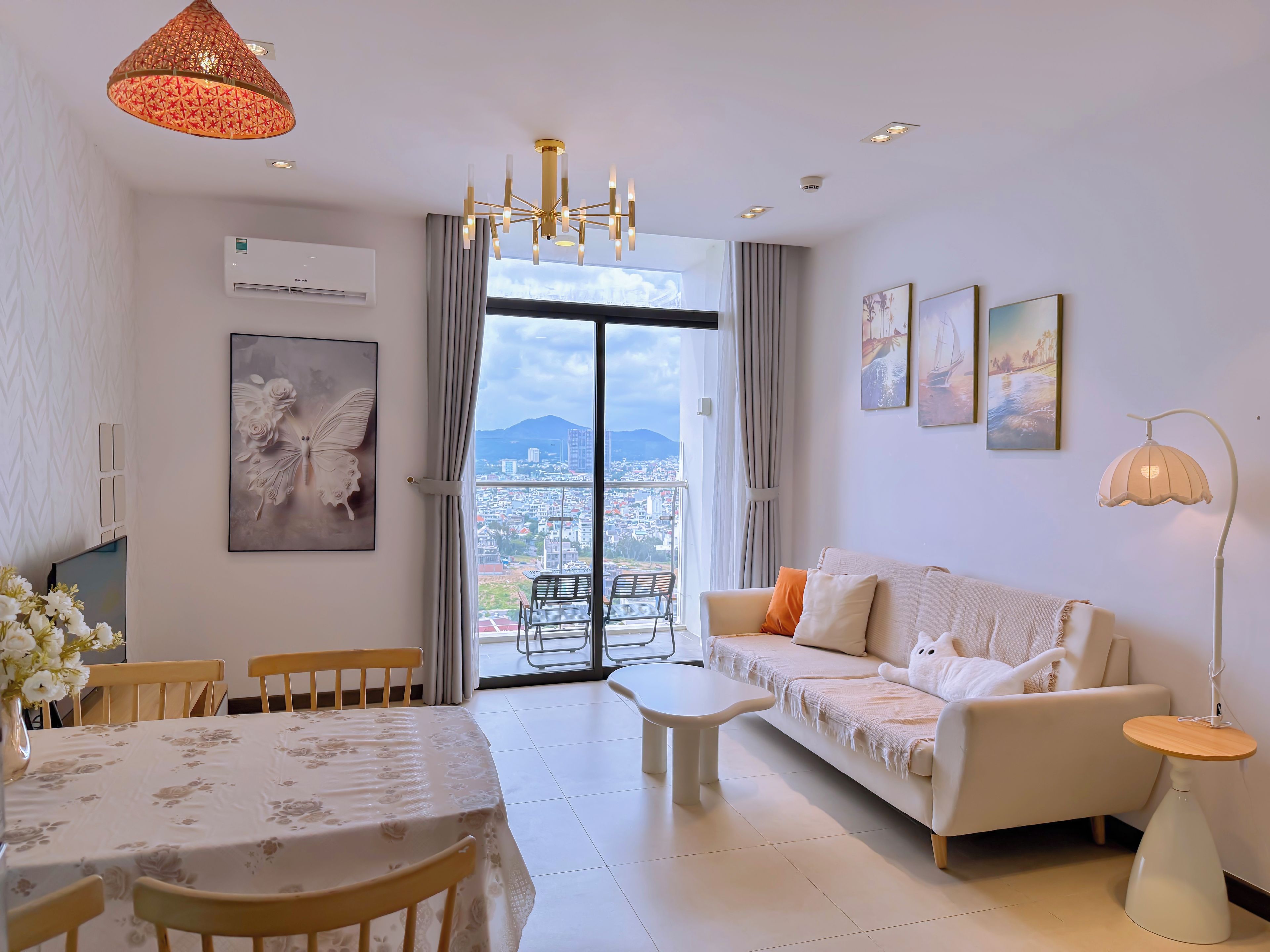 Una sala de estar moderna con sofá, mesa de comedor y sillas, un ventanal con vista a la ciudad y una araña.