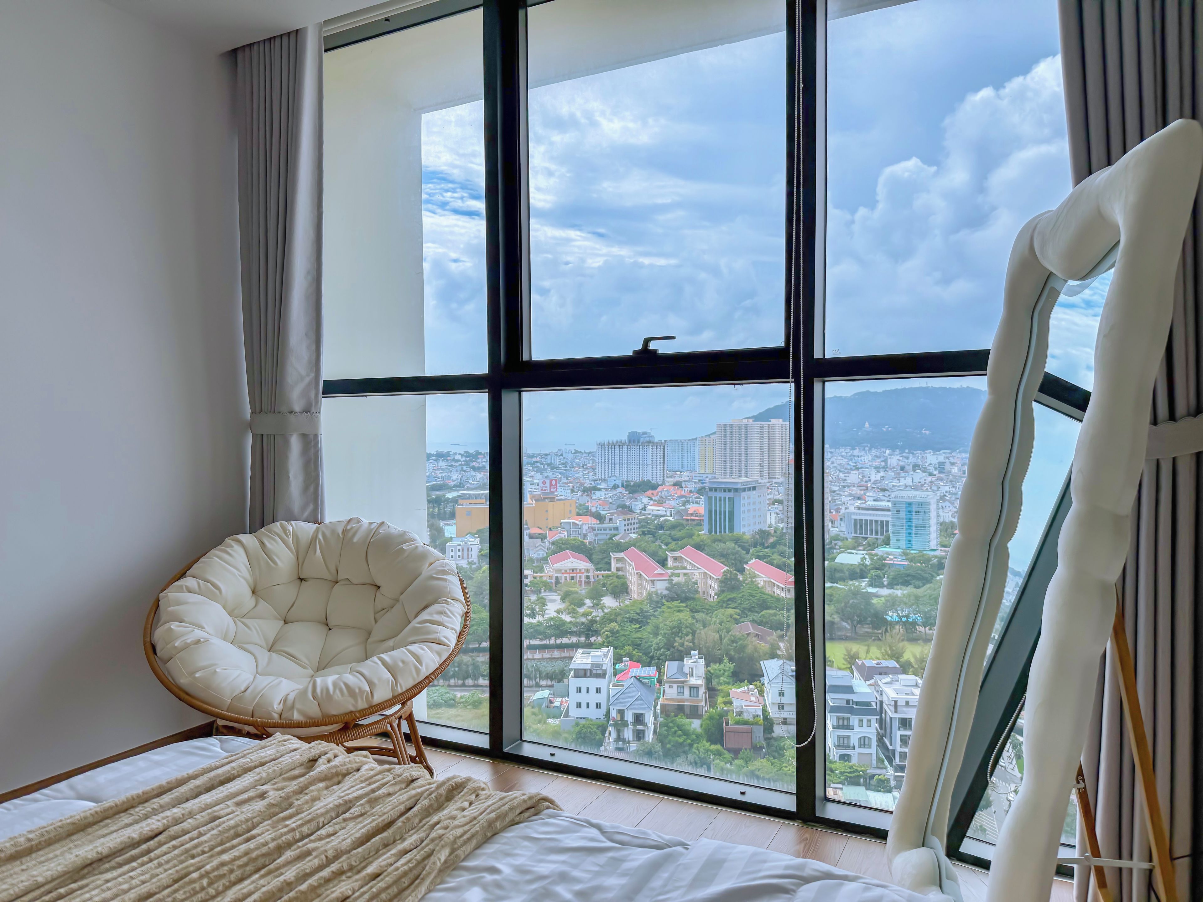 Une pièce avec une grande fenêtre, une chaise blanche et un lit recouvert d’une couverture blanche.