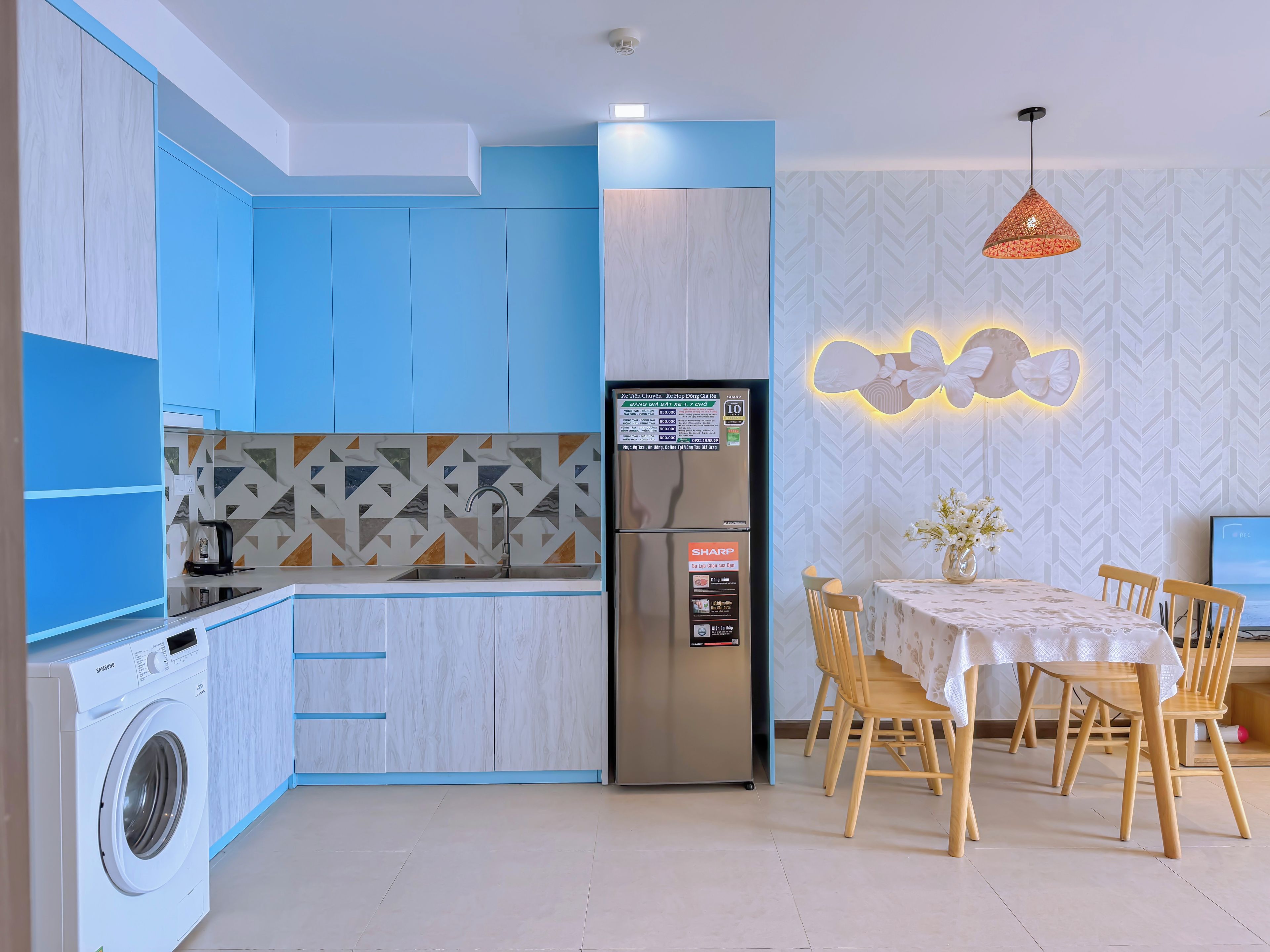 Una cocina moderna con armarios azules, lavadora integrada, refrigerador con pantalla digital y un comedor con mesa y sillas.