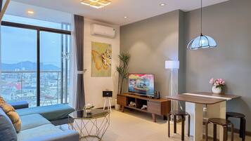 Una sala de estar moderna con un sofá, una mesa de centro, un televisor y un comedor con taburetes.