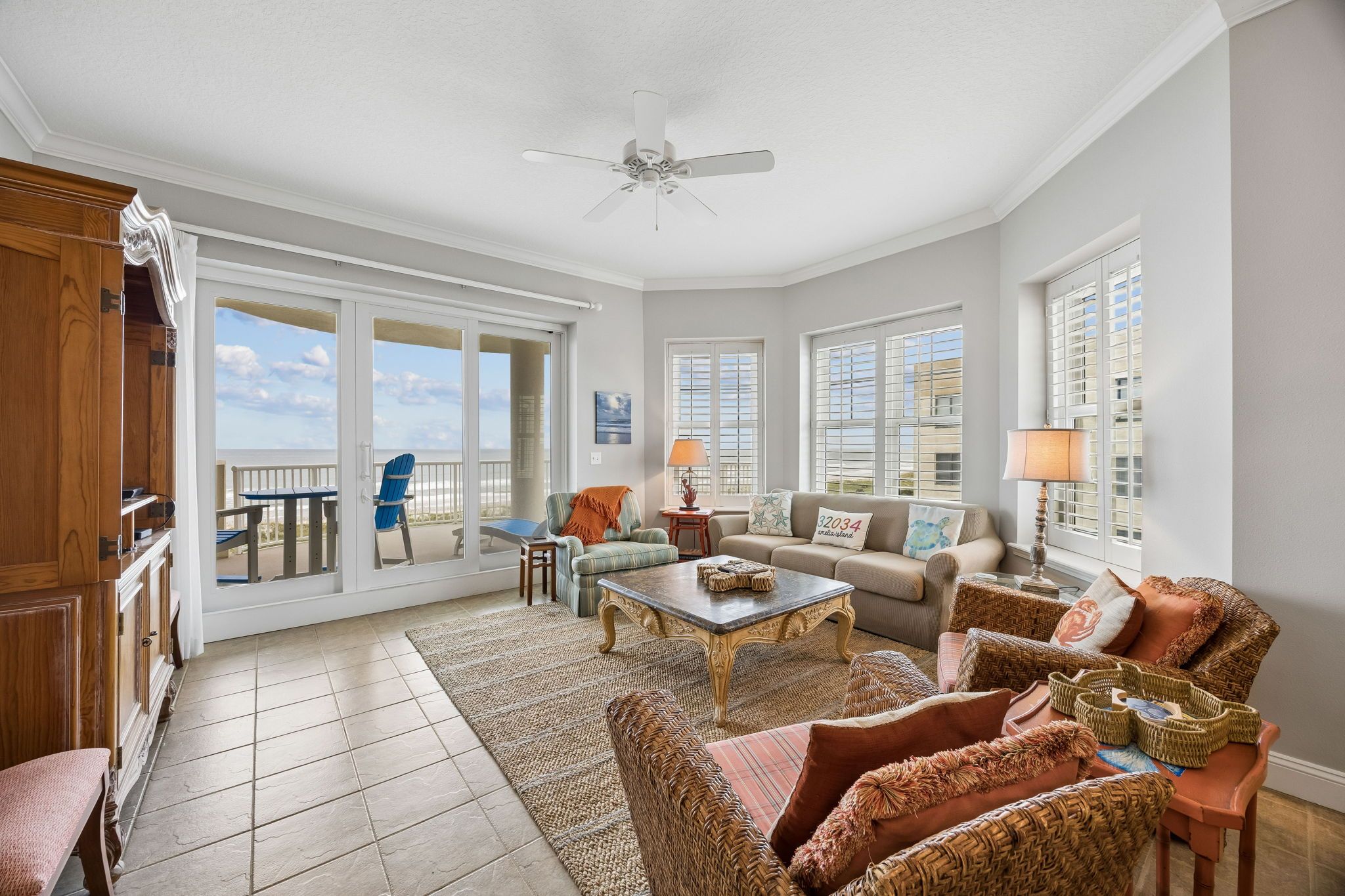 A spacious living room with a large window, a ceiling fan, and a view of the beach.