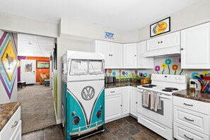 A kitchen with white cabinets, a vintage VW bus refrigerator, and a colorful flower mural on the wall. - Bertha's Bungalow - Sleeps 8/Dog-Friendly (Superior)