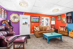 A vibrant living room with a brown leather sofa, a teal coffee table, and a purple wall with various framed artworks. - Bertha's Bungalow - Sleeps 8/Dog-Friendly (Superior)