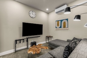 A modern living room with a flat-screen TV, a clock, and a decorative wall piece. - Turkey Trot Lodge | Private Hot Tub, 2 Miles to Downtown Leavenworth (Leavenworth)