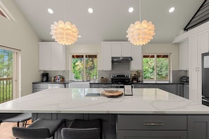 Una cucina moderna con un'isola grande, mobili bianchi e illuminazione a sospensione.