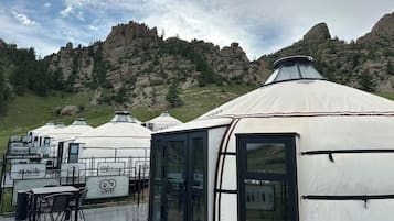 Yurtas con zona de comedor y mesas, con montañas al fondo.