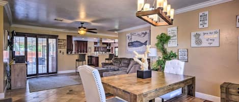A spacious living area with a dining table, a ceiling fan, and a kitchen in the background.