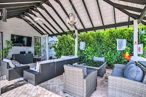 An outdoor covered patio with wicker furniture, a flat-screen TV, and a fire extinguisher. - Haze Estate: Weddings, Events, Pool, Lake & Bar (Bonita Springs)