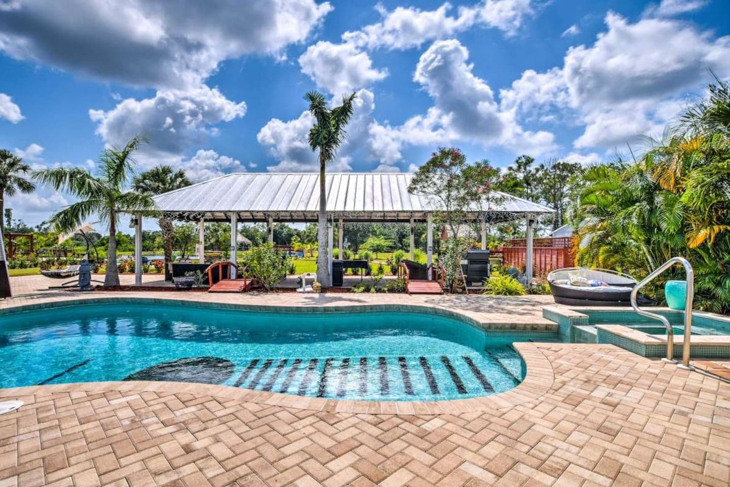 A swimming pool with a covered area, surrounded by palm trees and a clear sky.