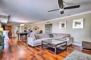 A spacious living room with a wooden floor, a large sofa, a glass coffee table, and a ceiling fan. - Haze Estate: Weddings, Events, Pool, Lake & Bar (Bonita Springs)