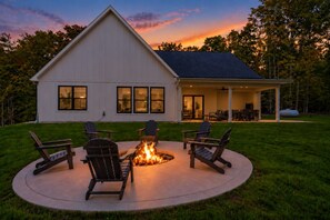 Ein Haus mit überdachter Terrasse, einem Feuerkorb und Sitzgelegenheiten im Freien.
