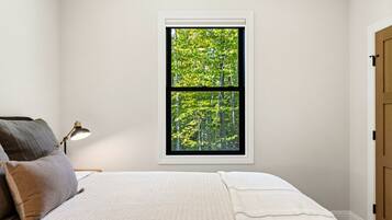 A bedroom with a bed, pillows, a nightstand, a lamp, and a window with a view of trees.