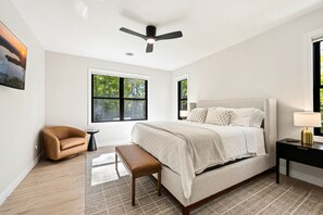 Ein Schlafzimmer mit einem großen Bett, einem Deckenventilator, einem Fenster mit Blick auf Bäume, einem braunen Ledersessel und einem kleinen Tisch.