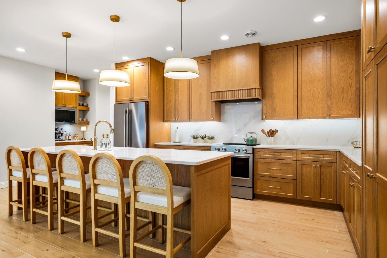 A modern kitchen with wooden cabinets, a stainless steel refrigerator, a gas stove, and a large island with bar stools.