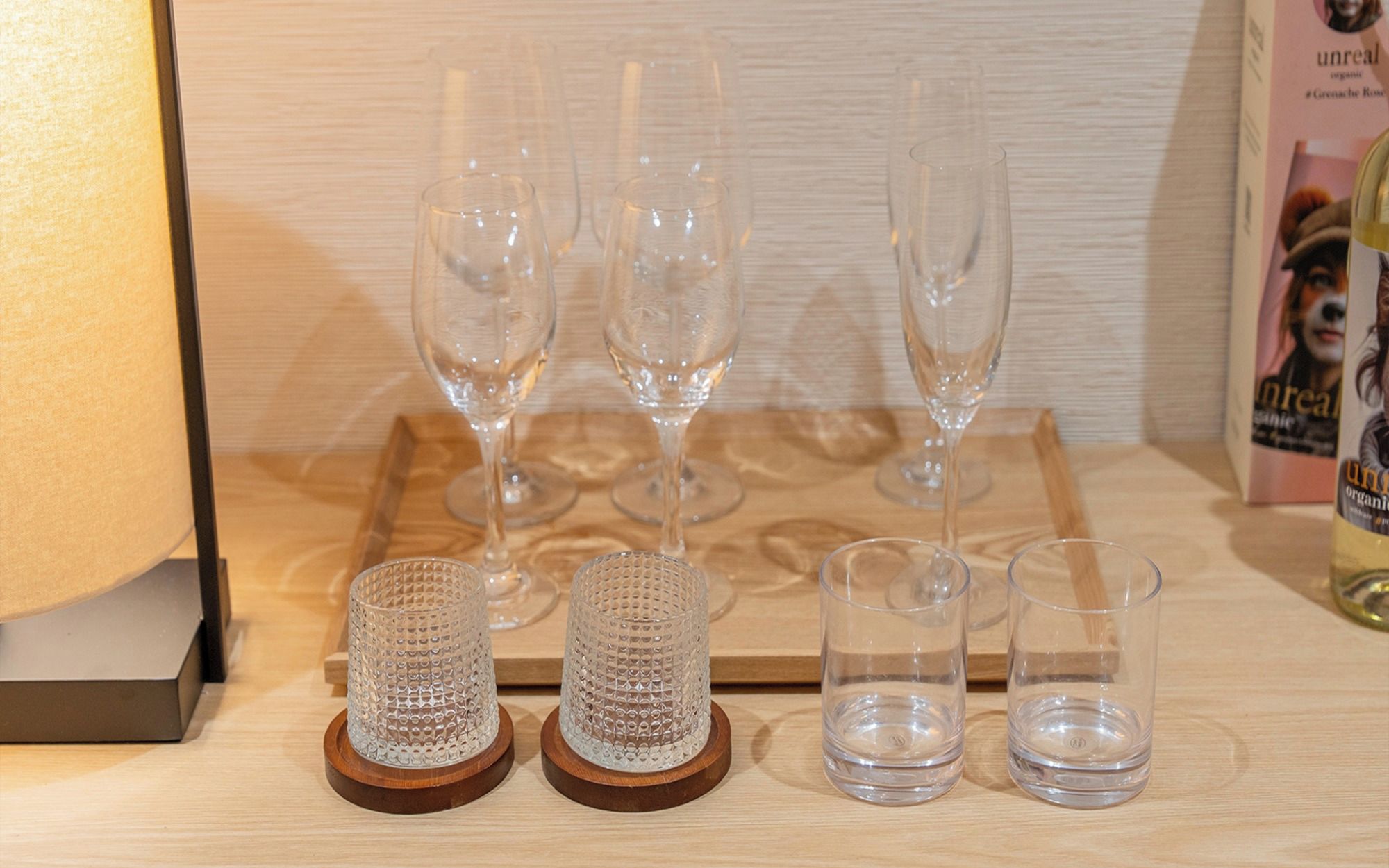 A wooden tray with four wine glasses and two small glass containers on a wooden surface.