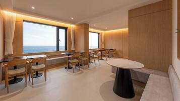 A modern interior with a seating area, tables, and a view of the sea.