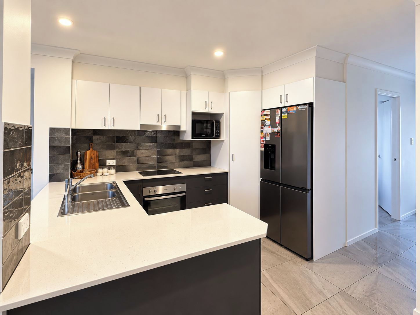 A modern kitchen with white cabinetry, a black refrigerator, and a black microwave.