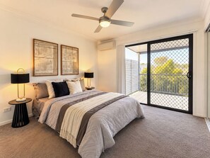 A bedroom with a bed, two bedside lamps, a ceiling fan, and a sliding glass door leading to an outdoor balcony. - Boondall 3BR Family Home | Long Stay Deals (Boondall)