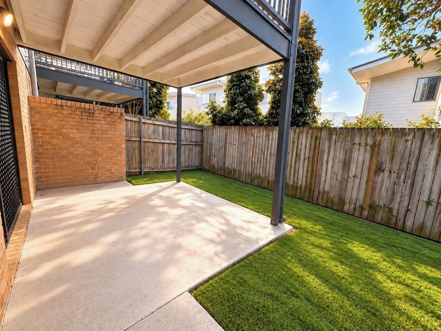A covered patio area with a brick wall, a wooden fence, and a well-maintained lawn.