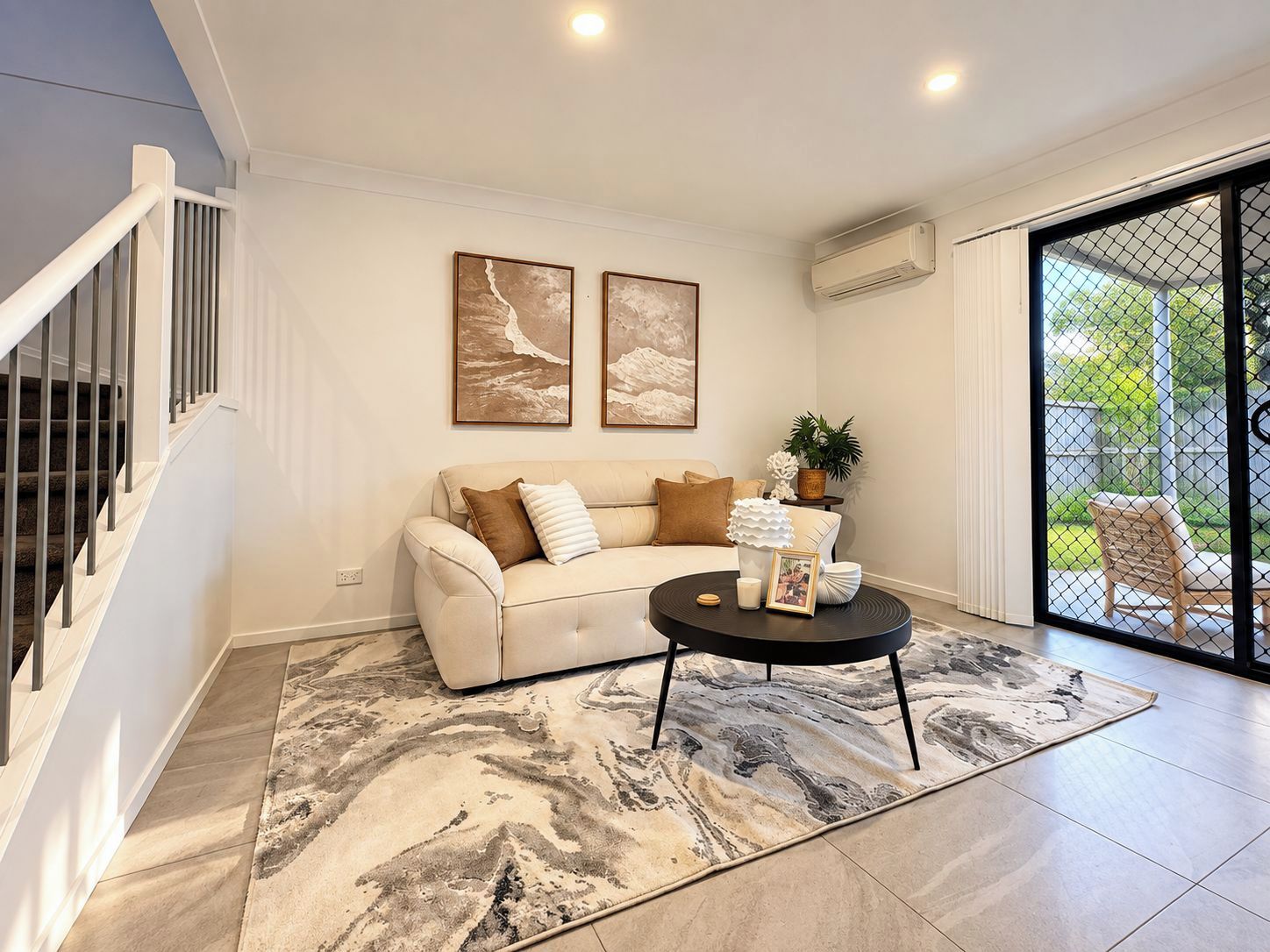 A modern living room with a staircase, a sofa, a coffee table, and a large window with a view.