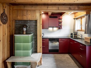 A compact kitchen with a green stove, red cabinets, and a wooden bench. - Mountain View Vals by Interhome (Vals)