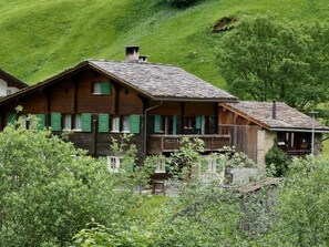 A traditional wooden chalet with a balcony, surrounded by lush greenery and a hilly landscape. - Mountain View Vals by Interhome (Vals)