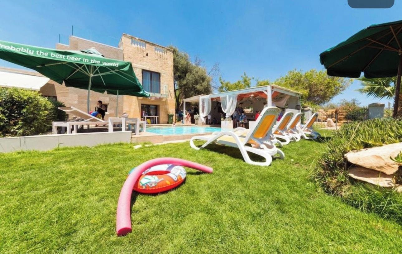 Un espace piscine avec des chaises longues et des parasols, une pelouse et un bâtiment portant une enseigne.