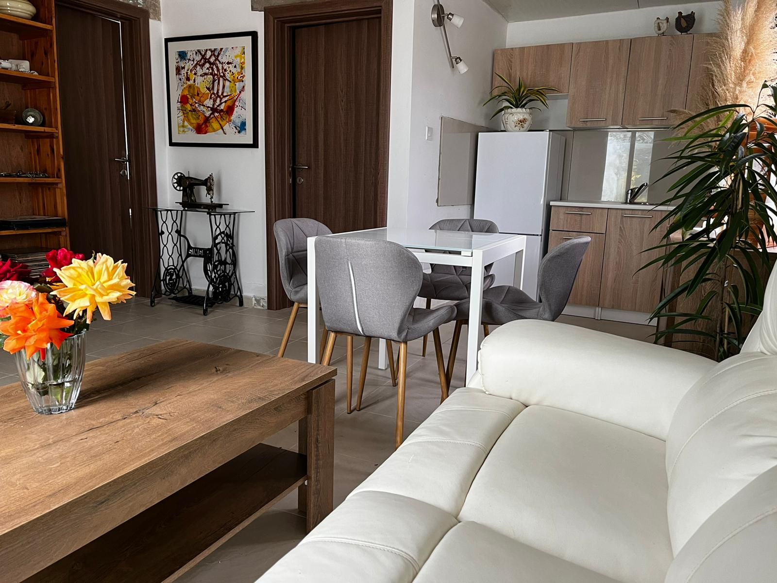 A modern living room with a sofa, dining table, chairs, and a vase of flowers.