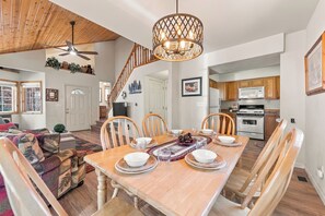 A dining area with a wooden table set for six, surrounded by chairs. A chandelier hangs above the table, and a staircase with wooden railings leads to an upper level. - Little Pinecone Retreat close to Rec Center (Truckee)
