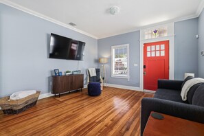 Ein Wohnzimmer mit einem Flachbildfernseher, einer roten Tür und einem Fenster mit Jalousien.