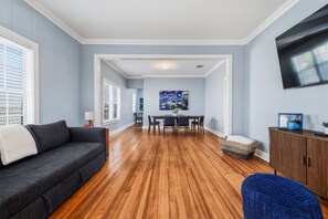 A living room with a dark grey sofa, wooden flooring, a dining area with a table and chairs, and a TV mounted on the wall. - Starry Night - A Birdy Vacation Rental (San Antonio)