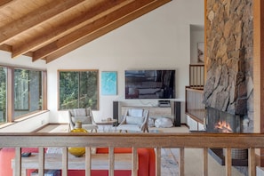 Ein modernes Wohnzimmer mit Kamin aus Stein, großen Fenstern und einem Fernseher.