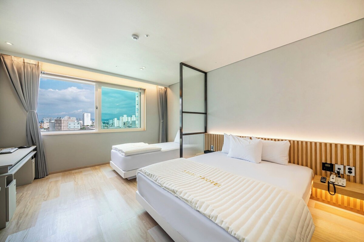 Una habitació d'hotel amb un llit gran, escriptori, cadira, finestra amb cortines i vista a la ciutat.