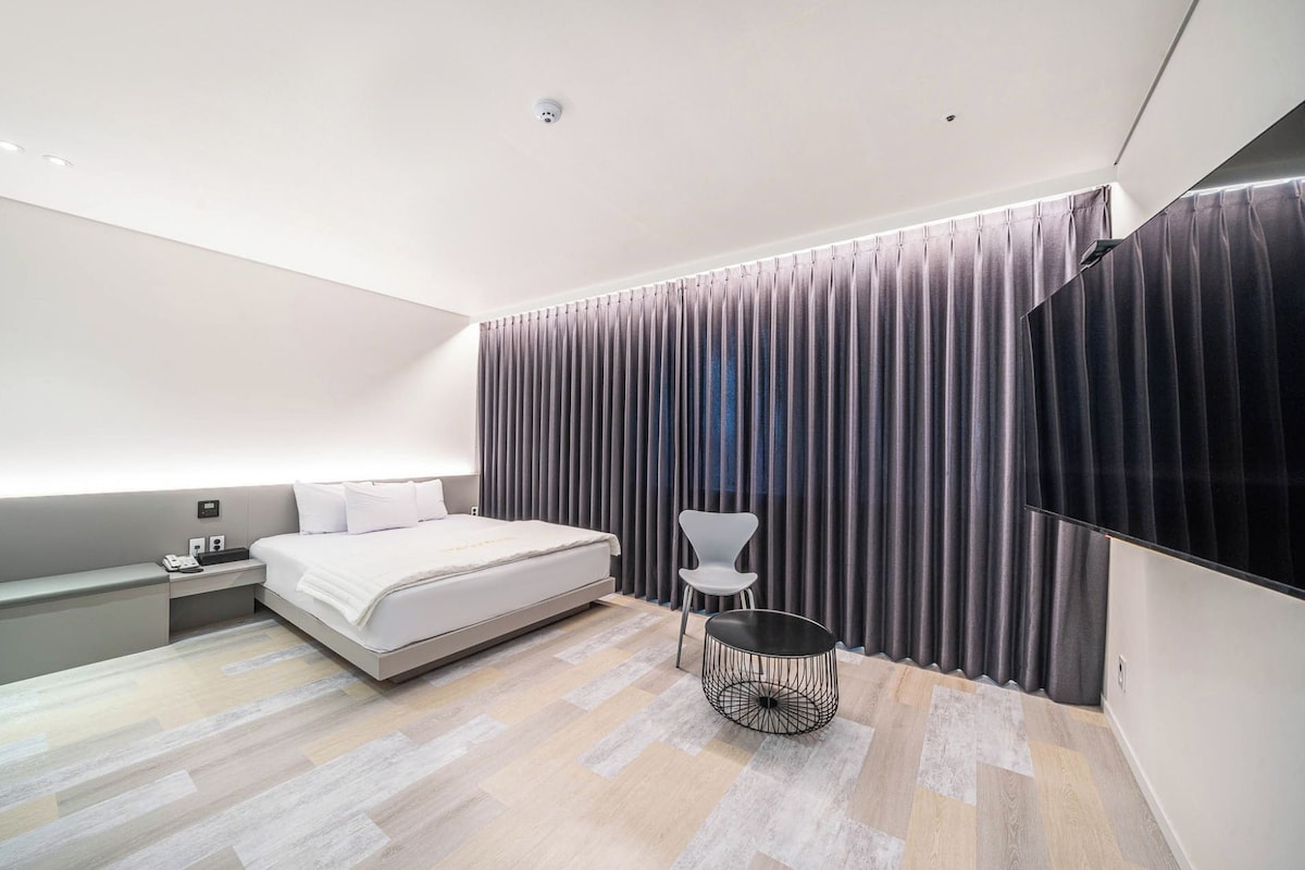 Una habitació d'hotel moderna amb llit, taula de nit, cadira i televisió de pantalla plana.