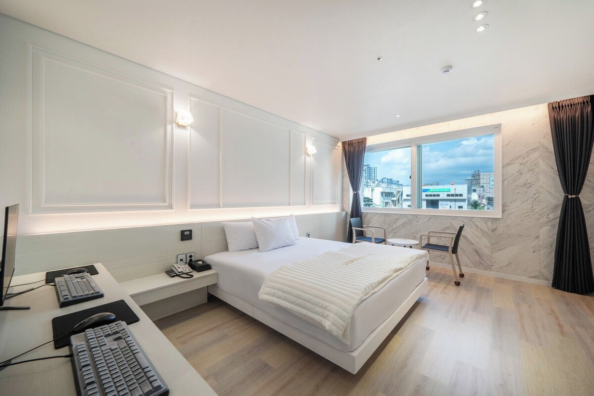 Habitació d'hotel moderna amb llit, escriptori i vista a la ciutat.