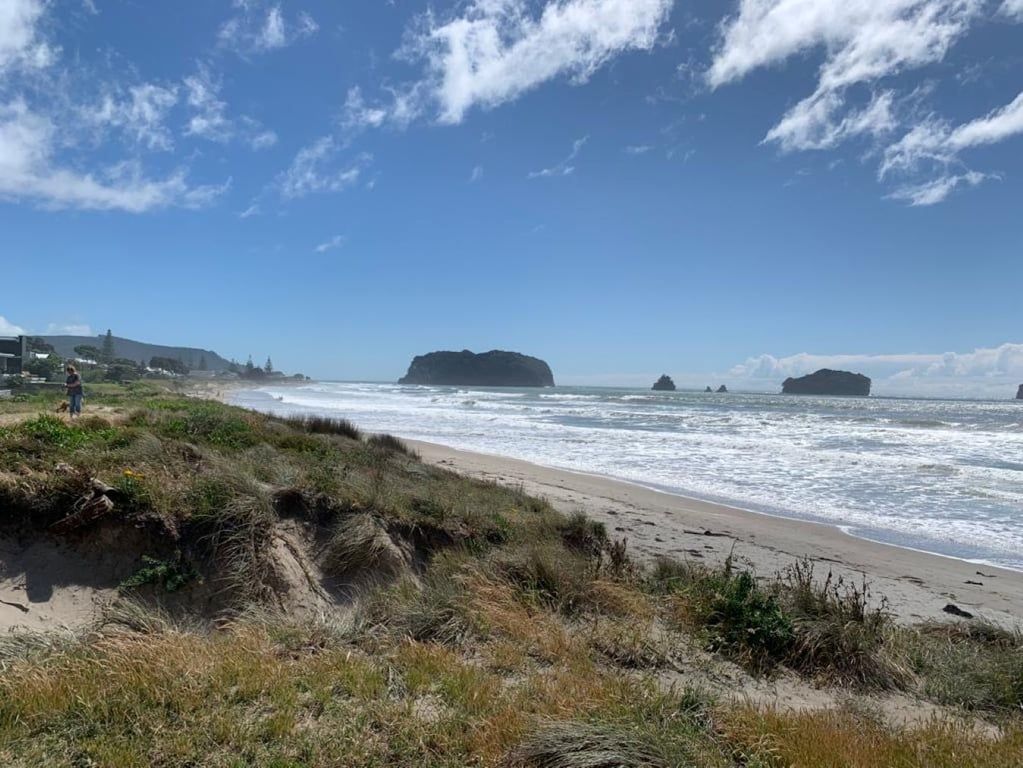 A beach with a clear sky, waves, and rocky outcrops.