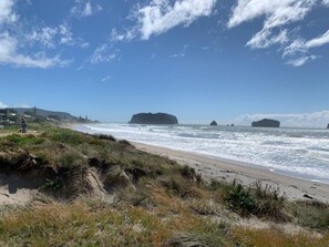 A beach with a clear sky, waves, and rocky outcrops. - The Hideaway @ Whanga (Whangamatā)