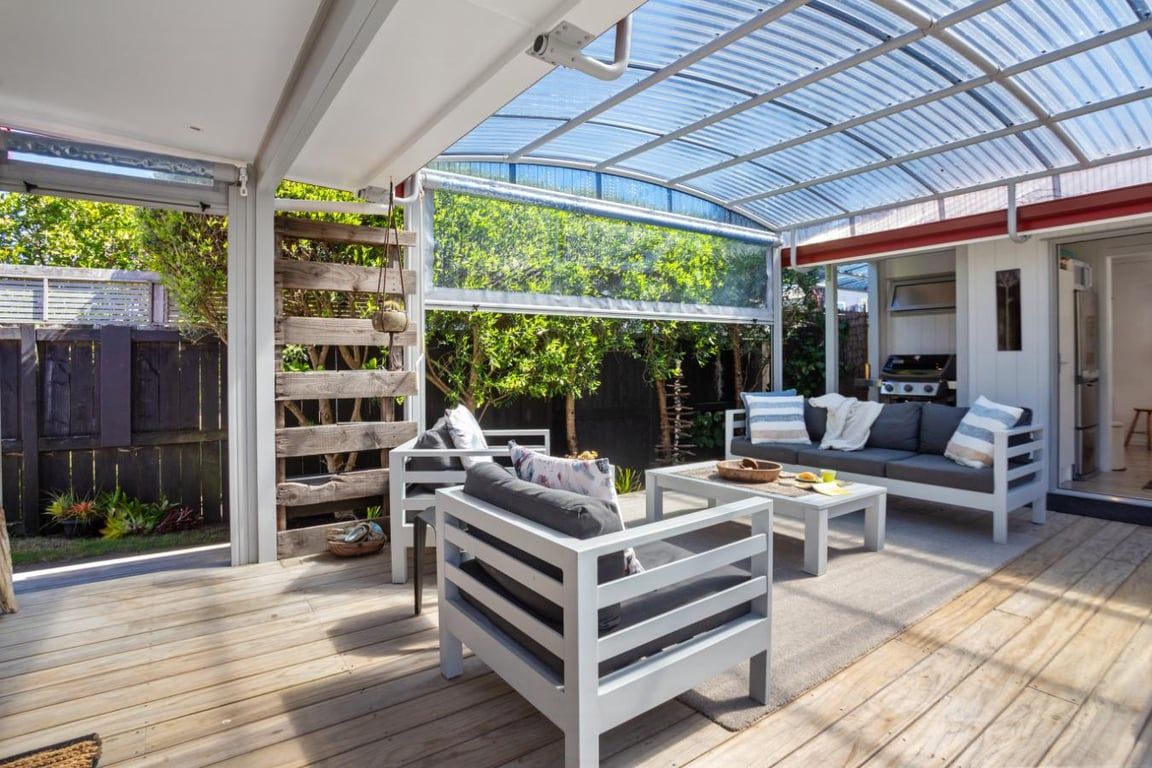 An outdoor patio with white furniture, a grill, and a glass-enclosed area with plants.