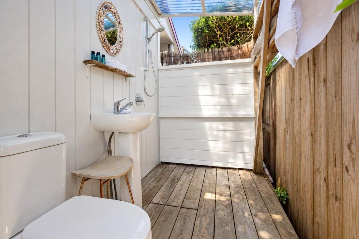 A small, enclosed outdoor bathroom with a toilet, sink, and shower.