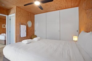 A bedroom with a large bed, a ceiling fan, a bedside lamp, and a wardrobe. - The Hideaway @ Whanga (Whangamatā)